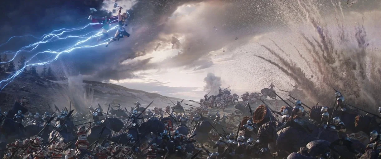 Thor: Love and Thunder (2022) movie still: wide — A vast, dusty battlefield swarms with soldiers fighting beneath a cloudy, overcast sky. Thor flies…