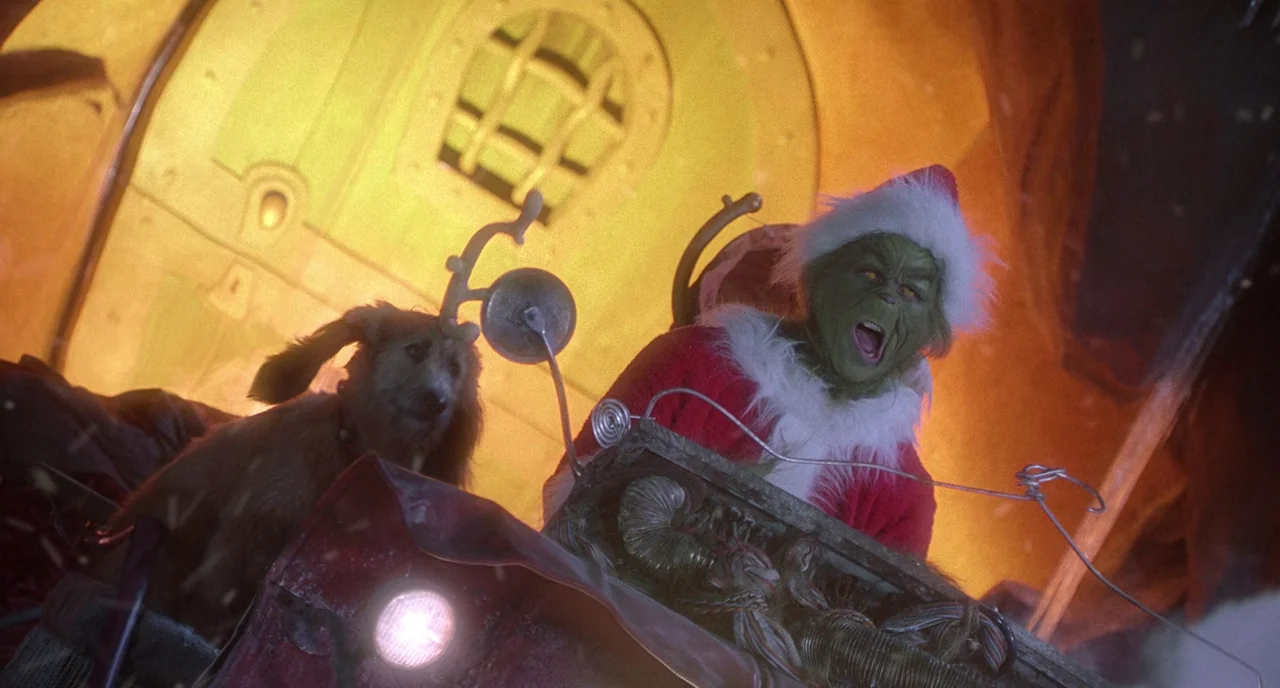 How The Grinch Stole Christmas (2000) movie still: medium — The Grinch and his dog sit inside a makeshift sled made of scrap metal. They are…