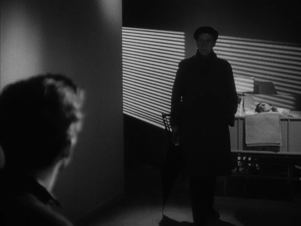 It Rains On Our Love (1946) movie still: medium — A dark hospital room with light streaming through venetian blinds on the wall. A man in an…