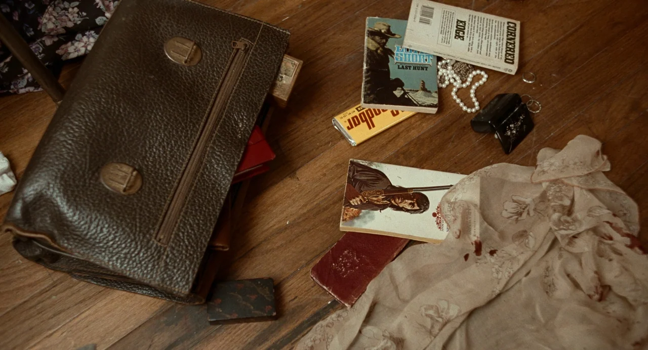 Bones and All (2022) movie still: wide — A collection of personal items is scattered across dark stained wooden floorboards. A leather briefcase,…