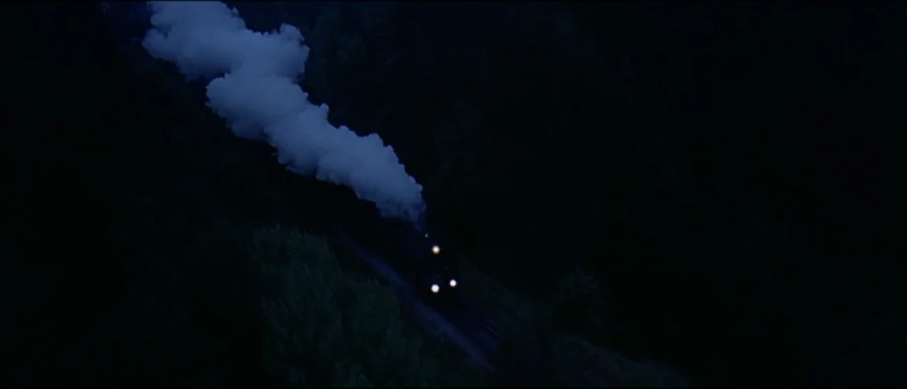 The Peacemaker (1997) movie still: wide — A steam locomotive cuts through a dense forest at night. Thick white steam trails behind the engine as it…