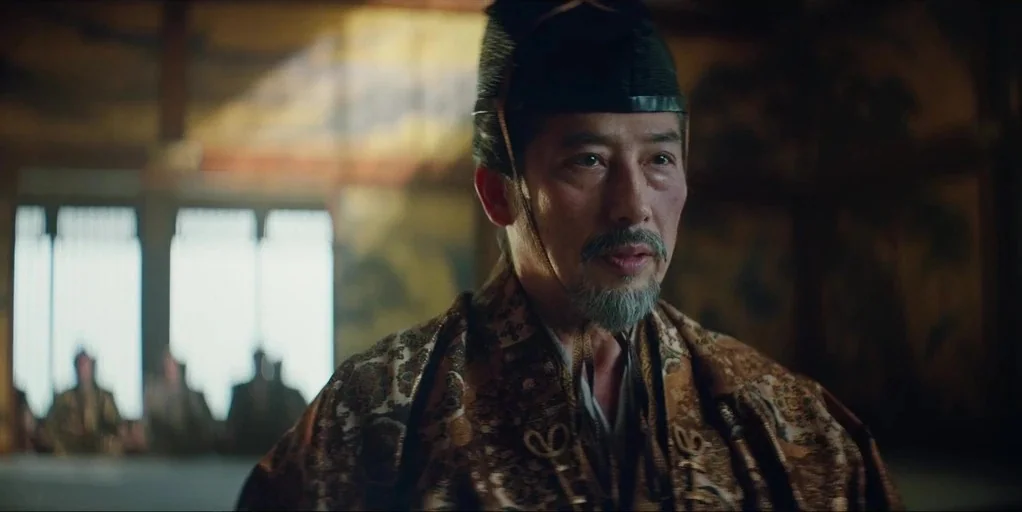 Shogun (2024) movie still: medium — A spacious hall features wood paneling and decorative painted screens in the background. An elderly man in…