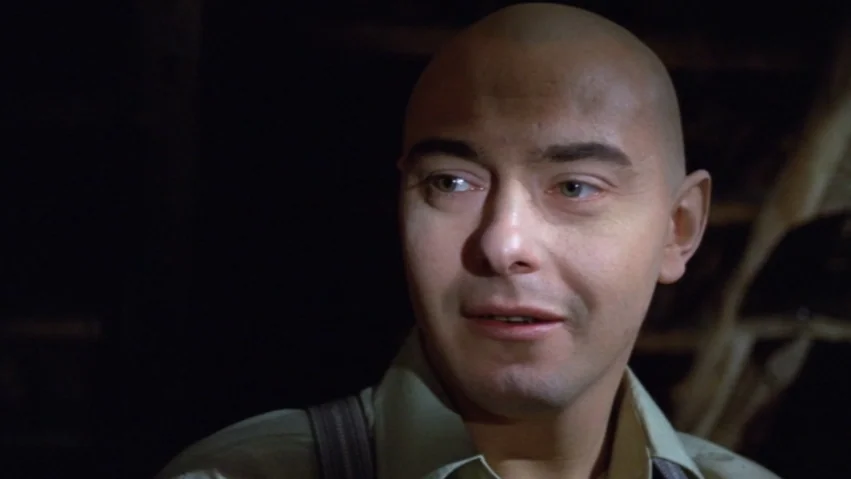 Tenderness of the Wolves (1973) movie still: closeup — A dimly lit interior space features a man in shadows. The man stares forward while turning…
