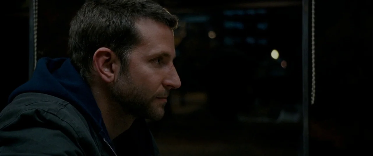 Silver Linings Playbook (2012) movie still: closeup — A dark vehicle cabin provides the setting for a man illuminated by dim light. The subject sits…