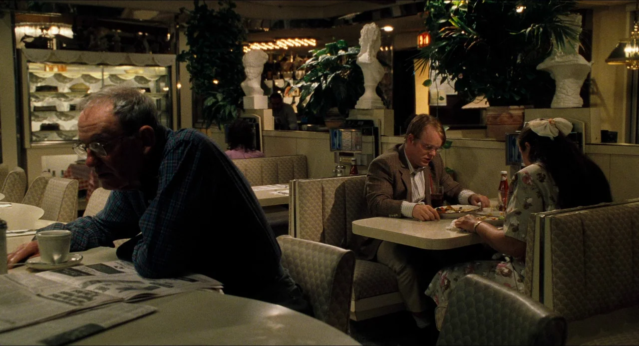Happiness (1998) movie still: wide — A quiet retro diner interior with upholstered booths and decorative plaster statues on partitions. One man sits…