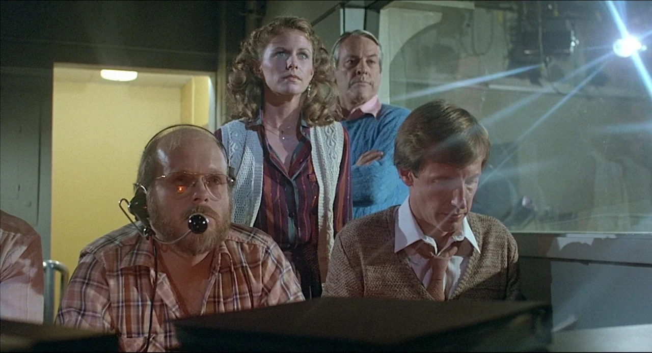 The Howling (1981) movie still: medium — A dimly lit technical workstation features several staff members observing electronic equipment at night.…