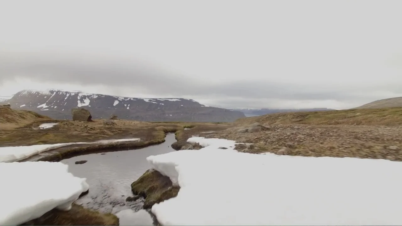 Iceland, the newborn island (2018) movie still: establishing — A vast Arctic tundra features a winding stream cutting through patches of melting…