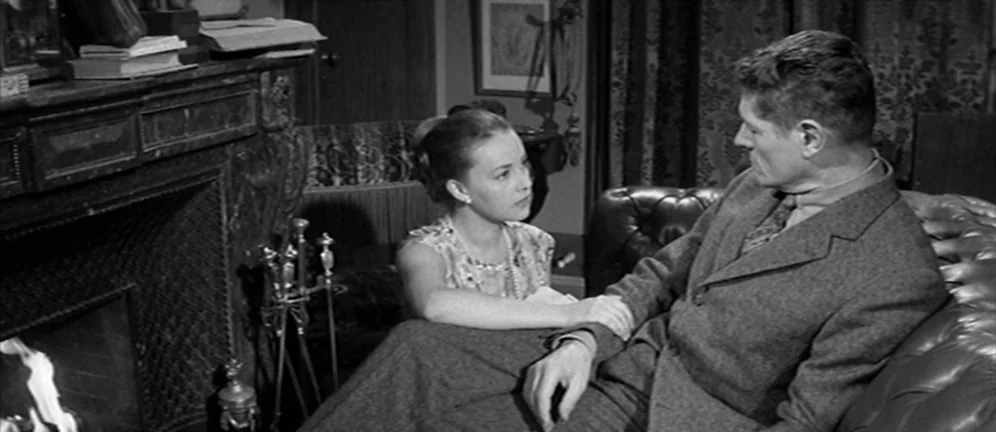 Les Amants (1958) movie still: medium — A traditional living room features a stone fireplace with a mantle and leather furniture. A woman sits on…