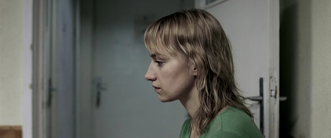 4 months, 3 Weeks and 2 Days (2007) movie still: medium — A woman stands in a plain interior doorway with white doors and neutral walls. The woman…