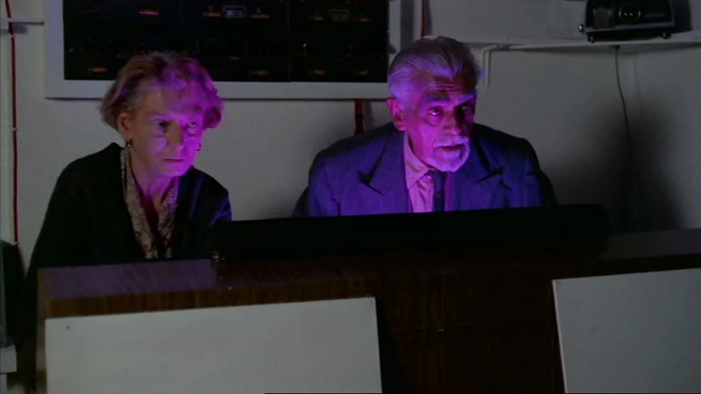The Sorcerers (1967) movie still: medium — A dimly lit room contains electronic equipment and panels against a white wall. Two older people sit…