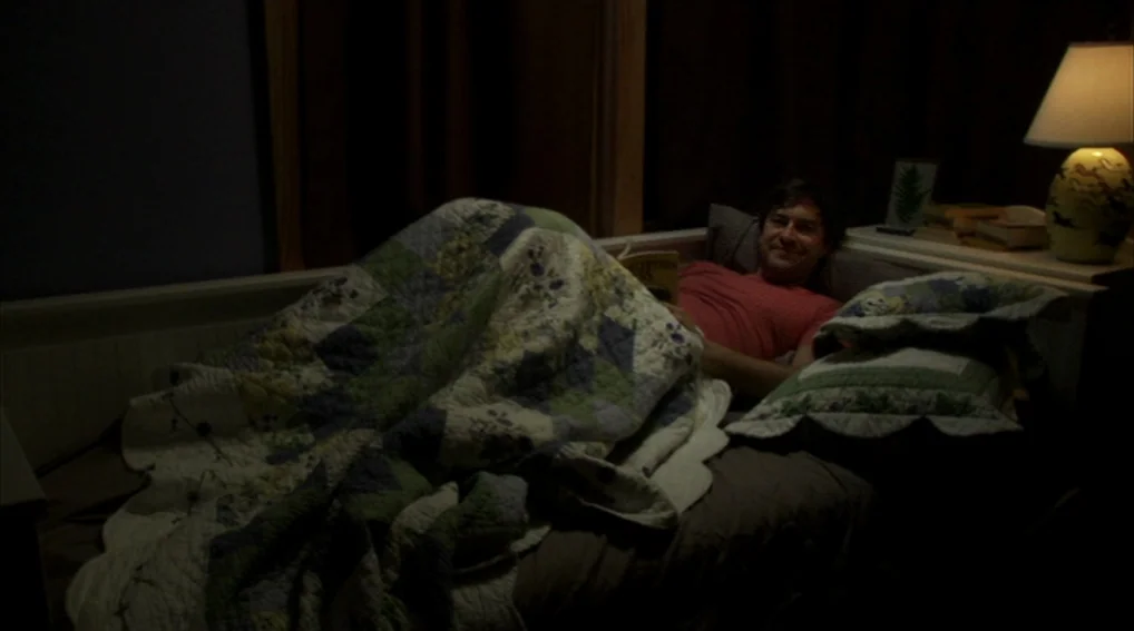 Your Sister’s Sister (2011) movie still: medium — A dark bedroom features a bed covered in a patterned quilt under dim illumination. A man lies in…