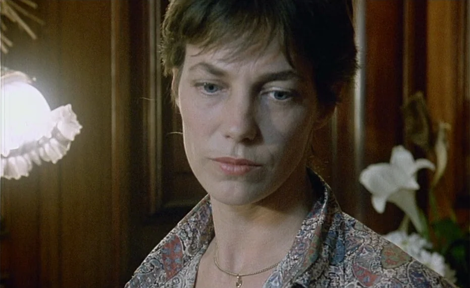 Jane B. par Agnès V. (1988) movie still: closeup — An interior space with dark wood paneling and white flowers on the right. A woman with short hair…