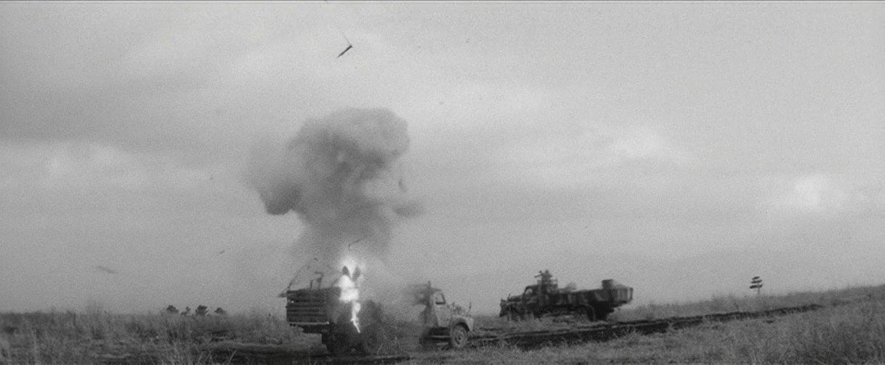 Story of a Prostitute (1965) movie still: wide — A desolate, flat grassy plain under an overcast sky features two military-style transport trucks.…