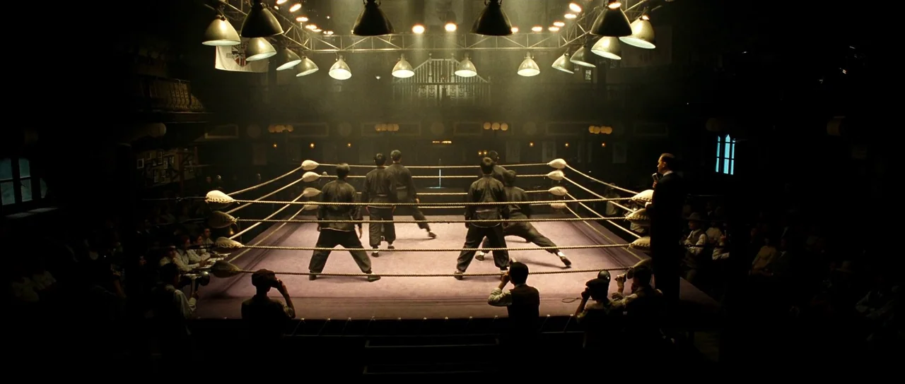 Ip Man 2 (2010) movie still: wide — A dimly lit indoor space featuring a central raised platform with thick rope barriers. Several men in dark…