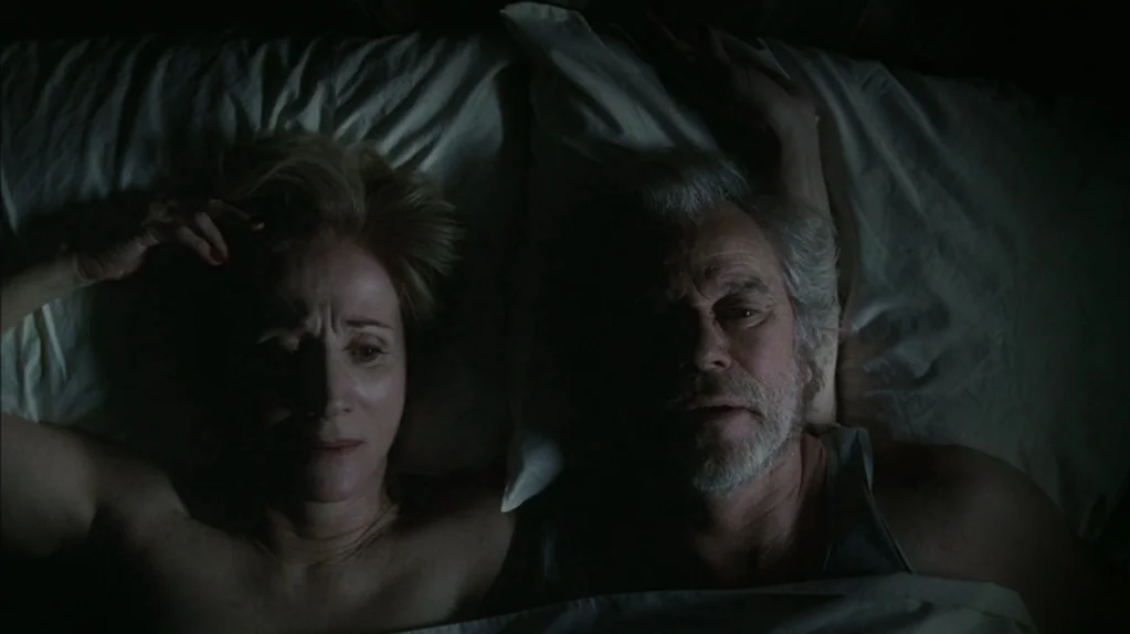 Away From Her (2006) movie still: closeup — An overhead view shows an older couple lying in bed in a dark room. The man wears a tank top and the…