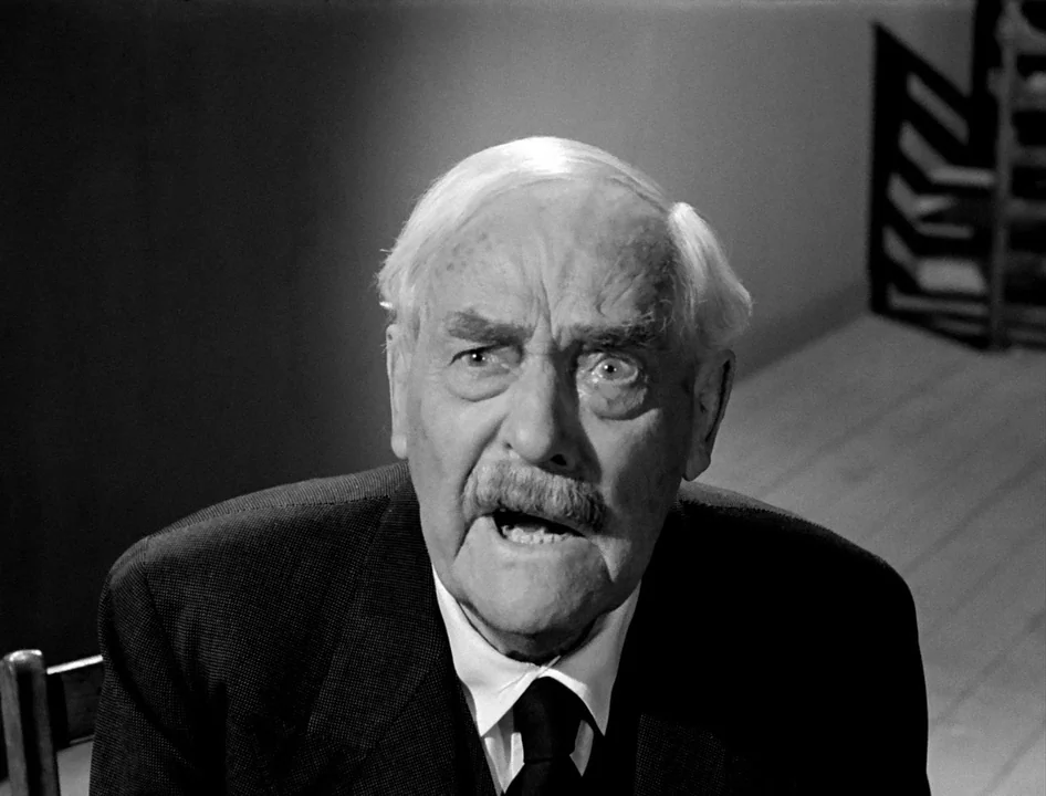 Wild Strawberries (1957) movie still: closeup — An elderly man in a suit looks upward against a stark, shadowed interior background. His mouth is…