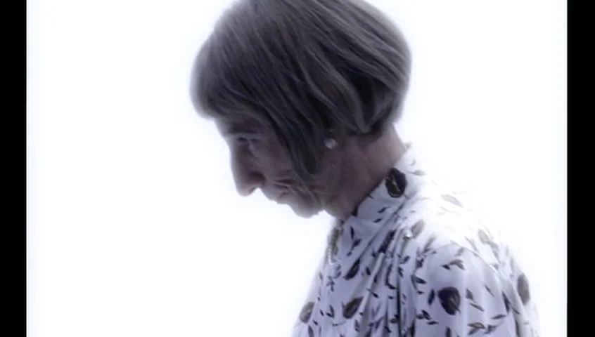 The Tracey Fragments (2007) movie still: closeup — An older woman stands against a completely overexposed white background. She is captured in…