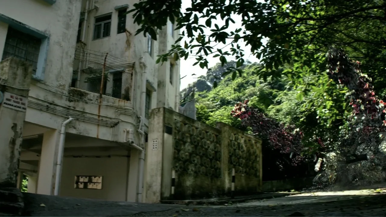 Transformers: Age of Extinction (2014) movie still: wide — An aging white apartment building stands next to a low concrete wall by trees. A road…