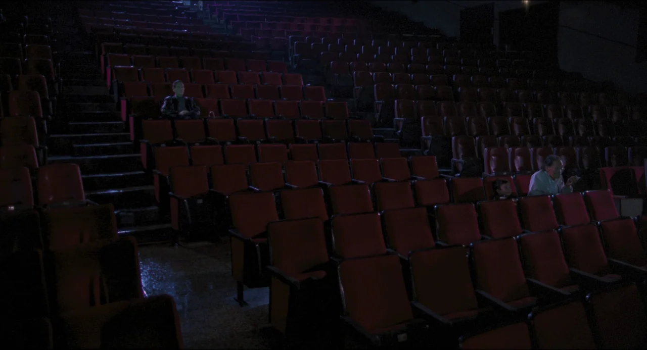Goodbye, Dragon Inn (2003) movie still: wide — A dark movie theater auditorium features rows of empty red cushioned seats. A few scattered…