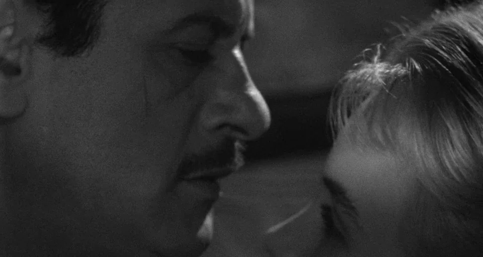 Baby Doll (1956) movie still: closeup — An dark interior space provides a background for two faces in close proximity. A man with a mustache faces a…