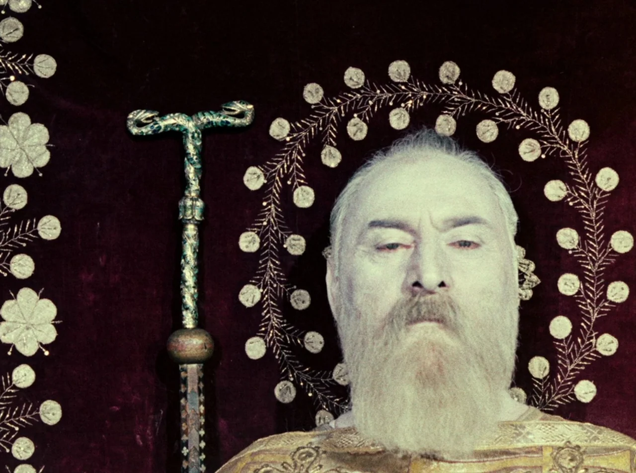 The Colour of Pomegranates (1969) movie still: closeup — A man with a white beard sits before a dark maroon velvet tapestry with embroidery. The…
