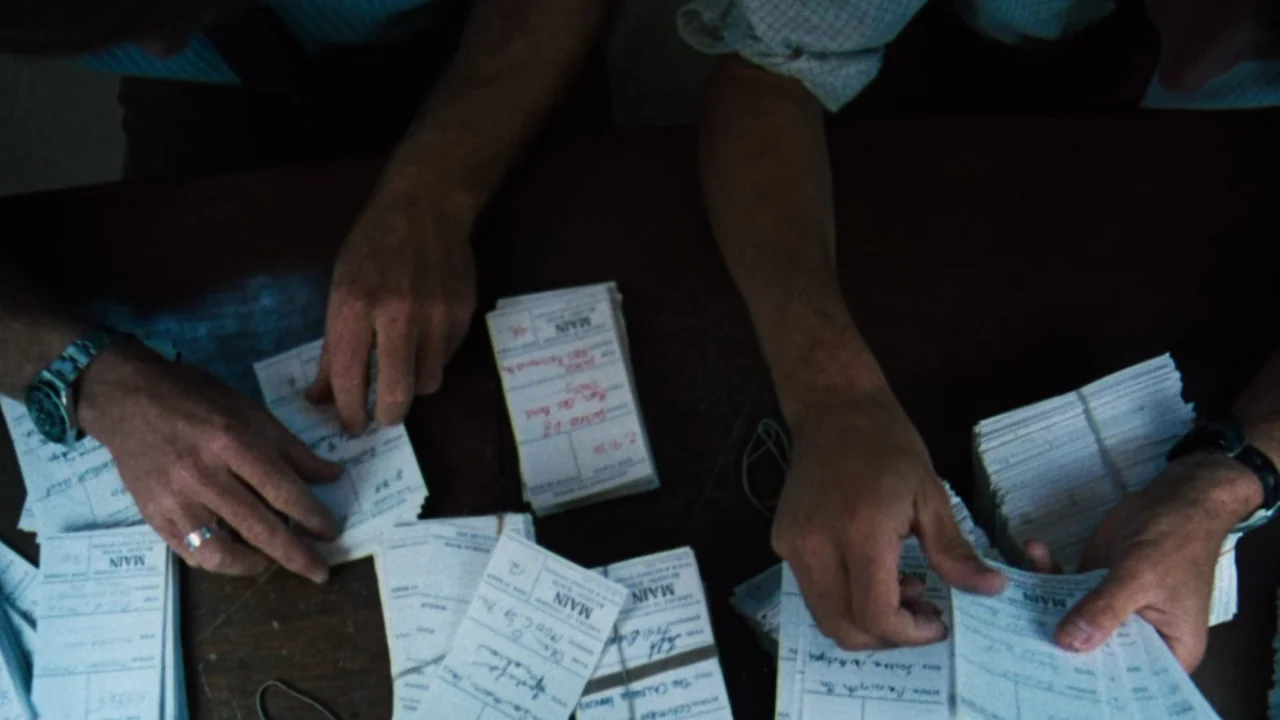 All the President's Men (1976) movie still: closeup — A wooden table surface is covered with numerous stacks of paper file cards. Two people use…