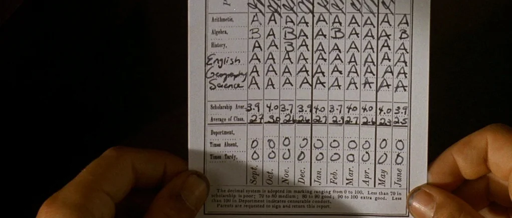 King of the Hill (1993) movie still: closeup — A close-up view of a printed report card held between two human hands. The paper features handwritten…