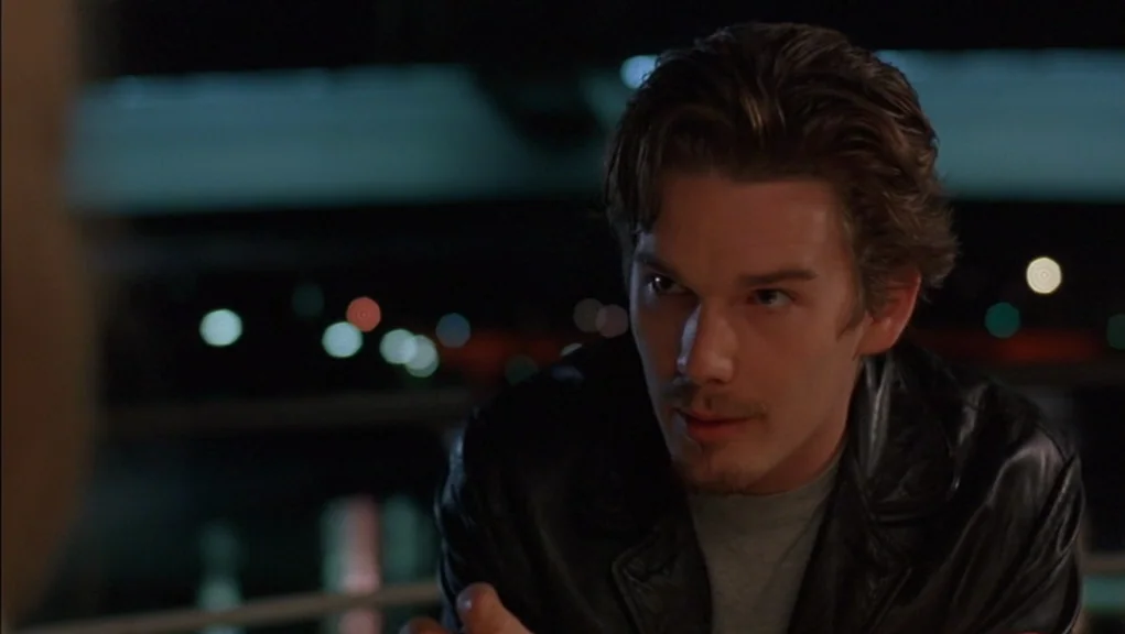 Before Sunrise (1995) movie still: medium — A man stands on a balcony at night with city lights blurred in background. He looks toward an unseen…