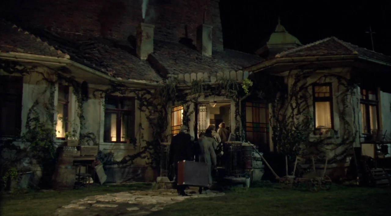 Underground (1995) movie still: wide — An aging, overgrown stucco cottage features climbing vines and a smoking stone chimney at night. A small…