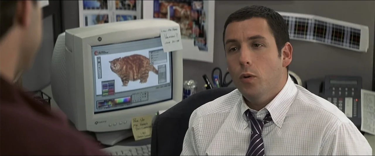 Anger Management (2003) movie still: medium — An office cubicle contains a computer monitor displaying an image of a cat. A man sits at his desk…