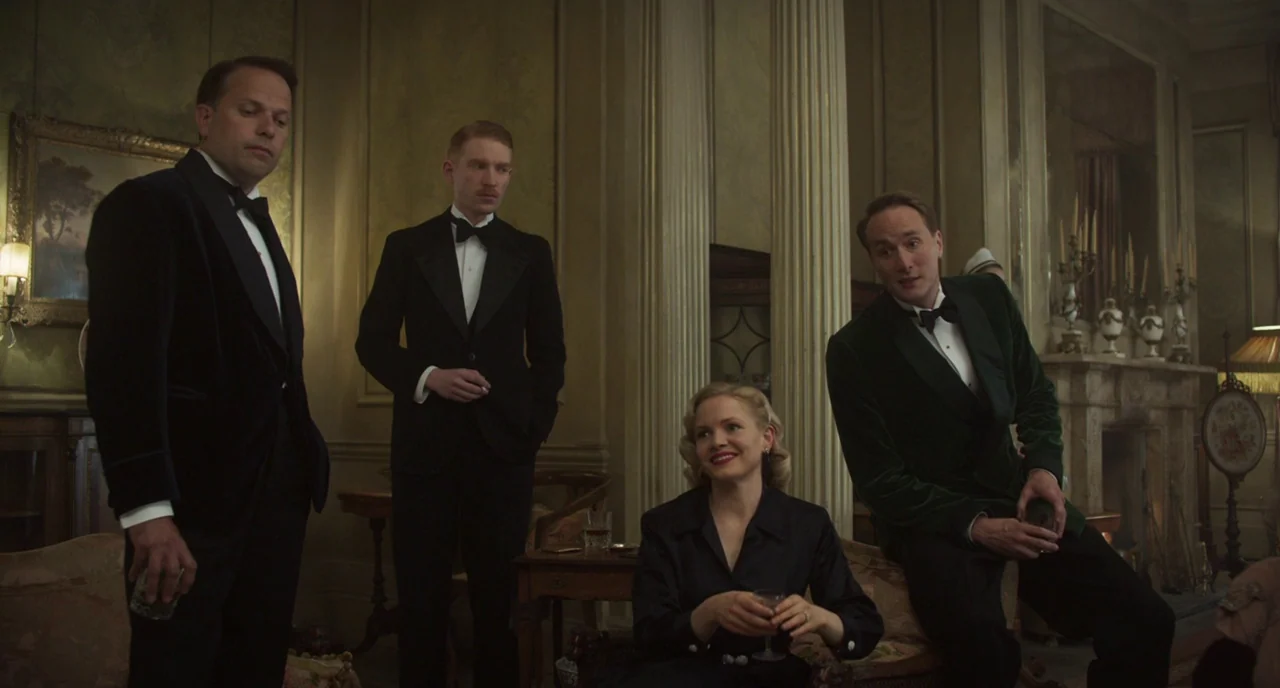 The Little Stranger (2018) movie still: medium — An opulent 1940s room features ornate moldings and a stone fireplace mantle. Four adults in formal…