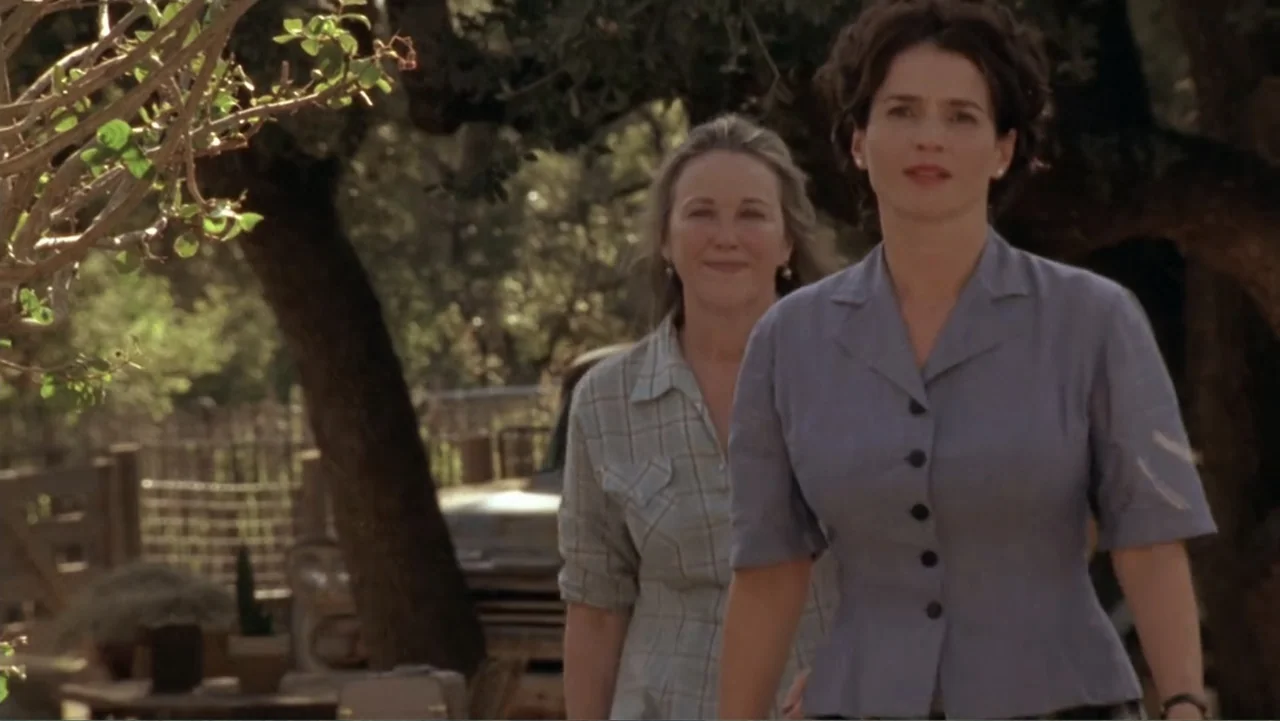 Temple Grandin (2010) movie still: medium — An outdoor area with large trees and a vintage truck in the background. Two women walk side by side…