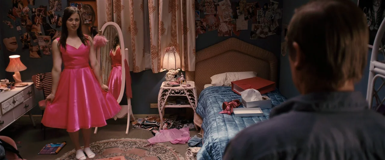 The Loved Ones (2009) movie still: fullbody — A teenage girl stands in a cluttered room filled with posters and clothes. The girl displays a new…
