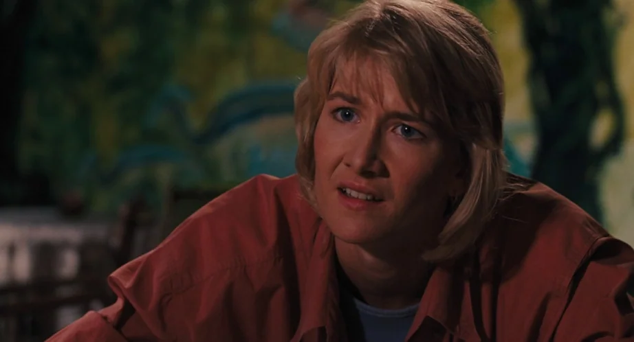 Jurassic Park (1993) movie still: medium — A dimly lit dining space features dark, abstract mural-like patterns on the back wall. A blonde woman in…
