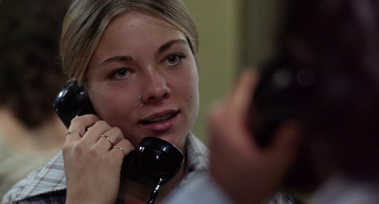 Straight Time (1978) movie still: closeup — An interior shot of a person using a vintage public telephone in a booth. The woman talks into the…