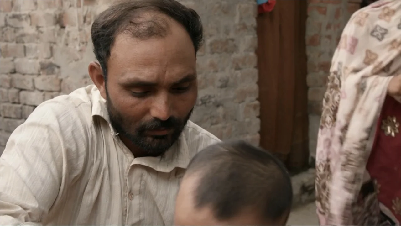 A Girl in the River: The Price of Forgiveness (2015) movie still: medium — An outdoor area with a textured brick wall serves as the background for…