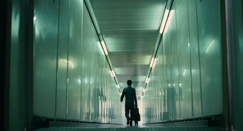 The Limits of Control (2009) movie still: wide — A long airport jet bridge stretches into the distance with reflective metallic side walls. A…