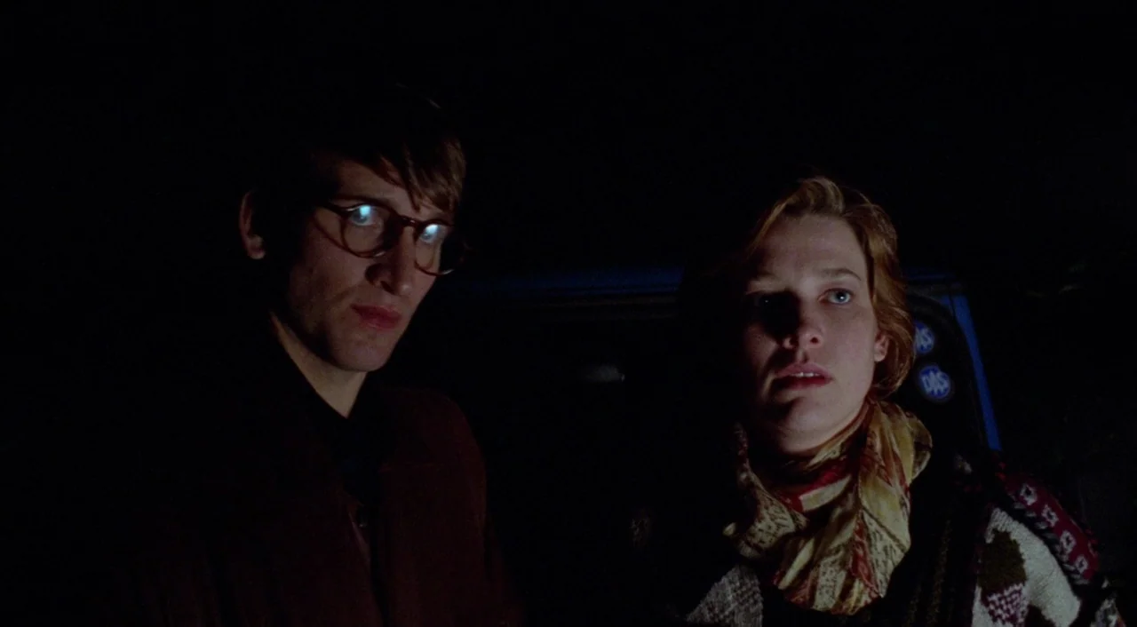 Shallow Grave (1994) movie still: medium — Two individuals sit in a dark vehicle at night illuminated by external light. The man wears glasses while…