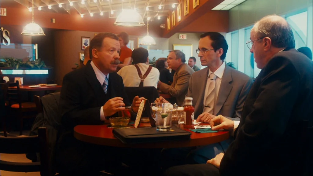 The Informant! (2009) movie still: medium — A group of businessmen sit around a circular table in a restaurant booth. The men are engaged in…