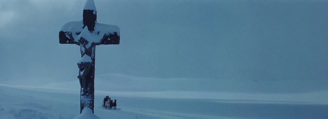 The Hateful Eight (2015) movie still: wide — A stone crucifix covered in snow stands in a vast, featureless frozen white landscape. A distant…