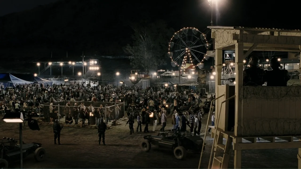 Tomorrow, When the War Began (2010) movie still: wide — A nighttime encampment at a fairground features a crowd of people gathered near a fence. A…