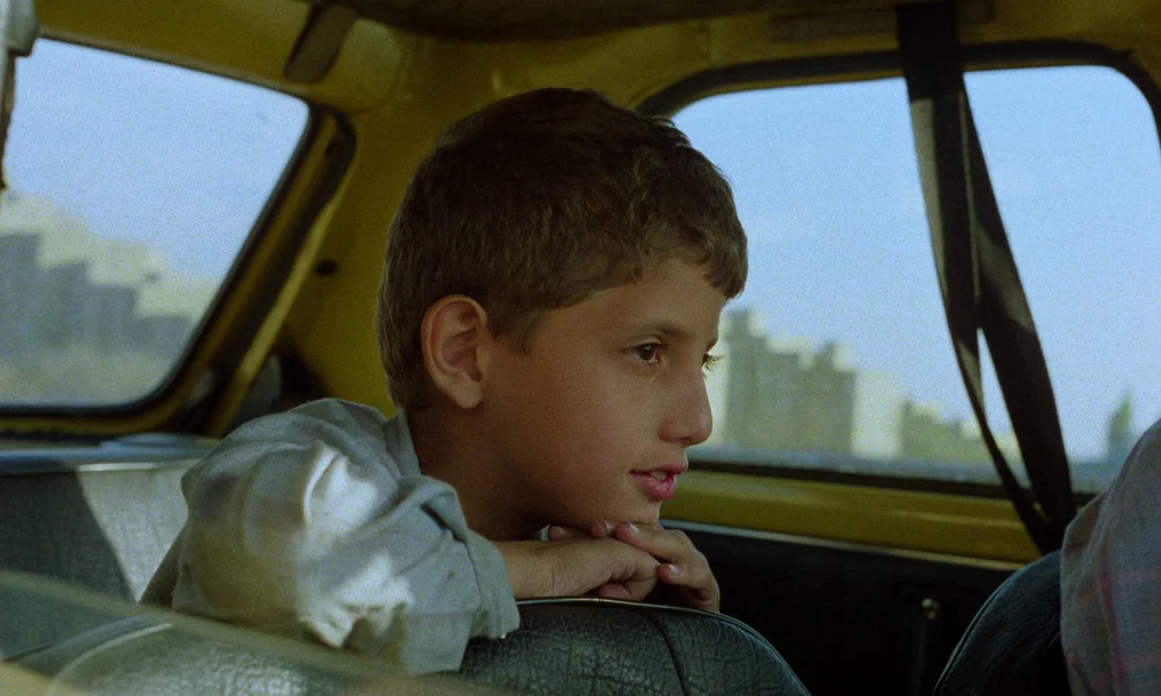 Life, and Nothing More (1992) movie still: medium — A boy sits in the backseat of a yellow car looking out the window. He rests his chin on his…