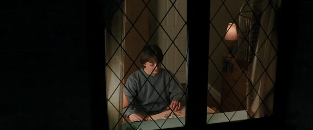 Harry Potter and the Chamber of Secrets (2002) movie still: medium — A young boy sits indoors at night behind a leaded glass diamond-pattern window.…