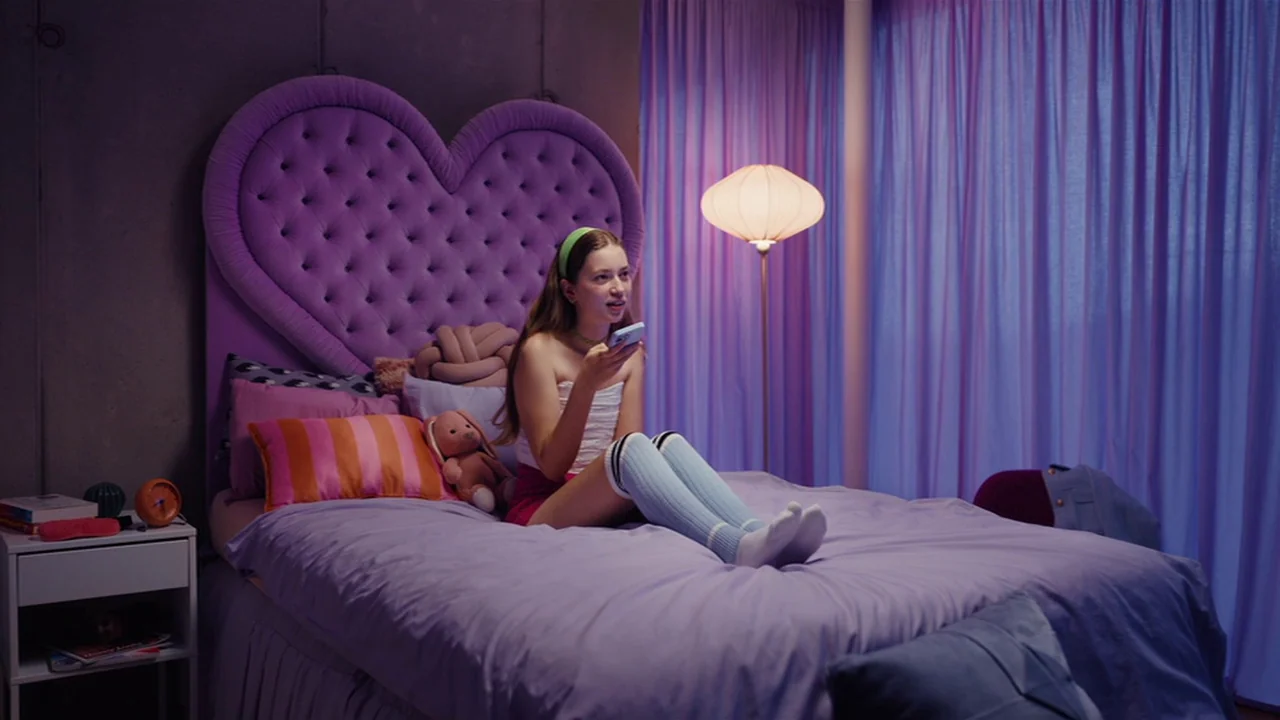 Club Zero (2023) movie still: medium — A room with a large heart-shaped purple headboard and flowing translucent curtains. The subject sits on the…