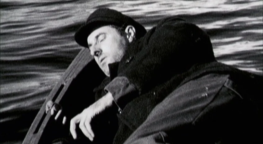 Brand Upon the Brain! (2006) movie still: medium — A man lies inside a small wooden boat on the water. The sunlight glares off the rippling water…