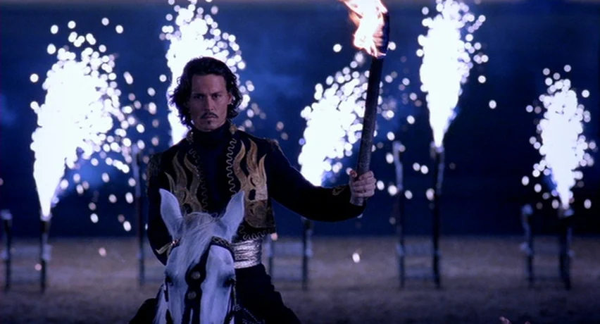 The Man Who Cried (2000) movie still: medium — A dark arena is illuminated by multiple vertical pyrotechnic displays and a single torch. A man in an…