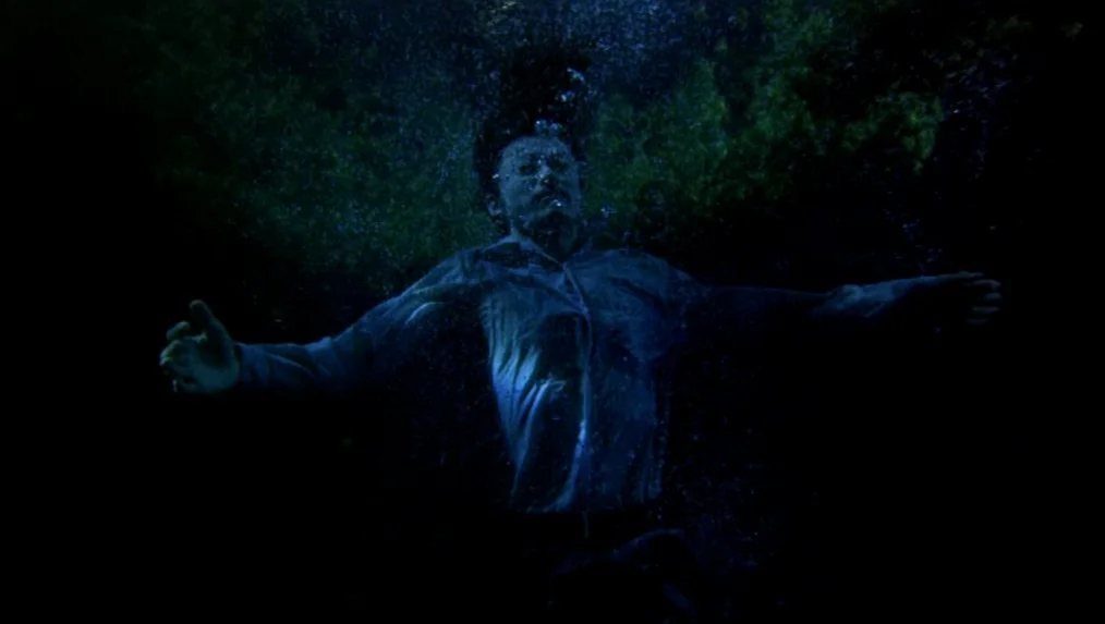 Last Life in the Universe (2003) movie still: medium — A man is submerged beneath the surface of dark, murky water at night. He floats motionless…