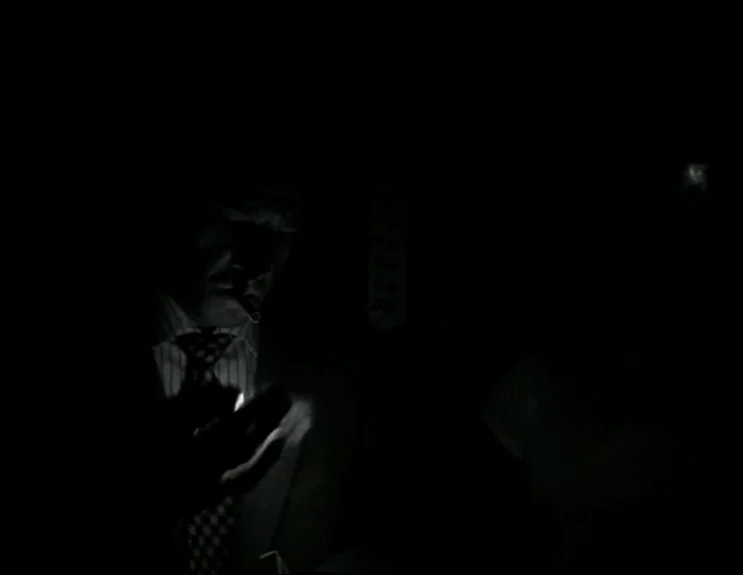 À Bout De Souffle (Breathless) (1960) movie still: closeup — A man stands in a dark, indistinct interior space. He holds a lit cigarette lighter…