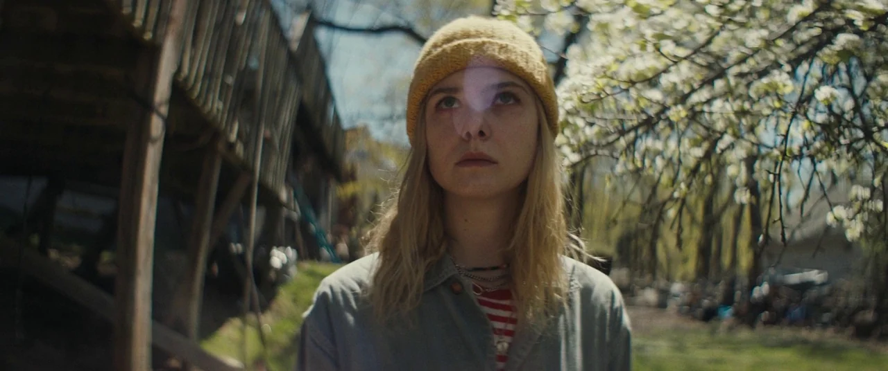I Think We’re Alone Now (2018) movie still: medium — A residential backyard features a wooden deck structure and a blooming dogwood tree. A young…