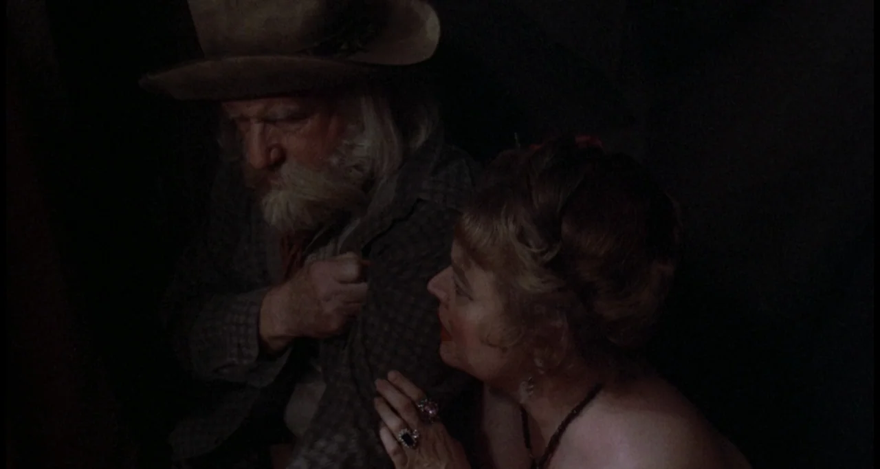 The White Buffalo (1977) movie still: medium — A dark interior space with minimal architectural detail visible in the shadows. An elderly man in a…